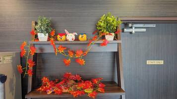 A hotel reception area with a wooden reception desk, a 'STAFF ONLY' sign, and decorative elements including potted plants and artificial flowers.