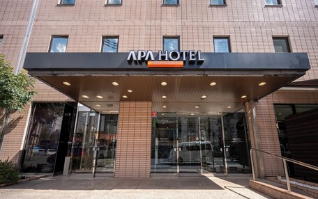 The entrance of APA Hotel with a modern design, featuring a glass facade and a covered entrance area.