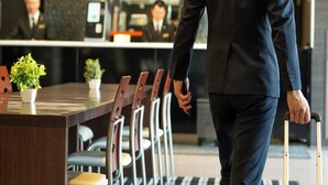 A man in a suit walking past a reception desk with a row of chairs and a potted plant. - APA Hotel Maebashieki-Kita (Maebashi)