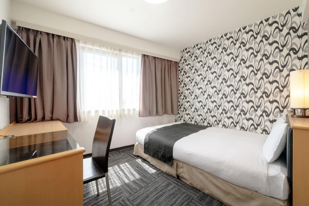 Une chambre d’hôtel avec un lit, un bureau, une chaise, une télévision et un mur décoré d’un motif.