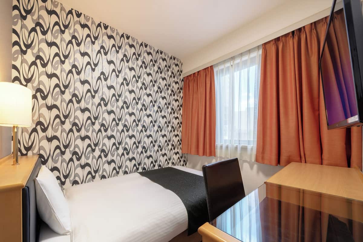 Une chambre d’hôtel équipée d’un lit, d’un bureau, d’une chaise, d’une lampe et d’un téléviseur.