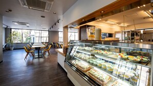 A modern dining area with a glass display case filled with various food items, a wooden table with chairs, and large windows allowing natural light. - APA Hotel Maebashieki-Kita (Maebashi)