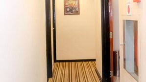 Een hotelhal met een gestreept tapijt, een schilderij aan de muur en een rookmelder aan de rechterkant.