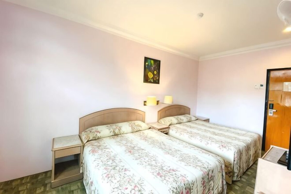 A hotel room with two beds, a nightstand, a wall-mounted lamp, and a door.