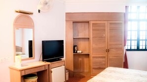 Een hotelkamer met een bed, een bureau met televisie, een kledingkast en een raam met gordijnen.