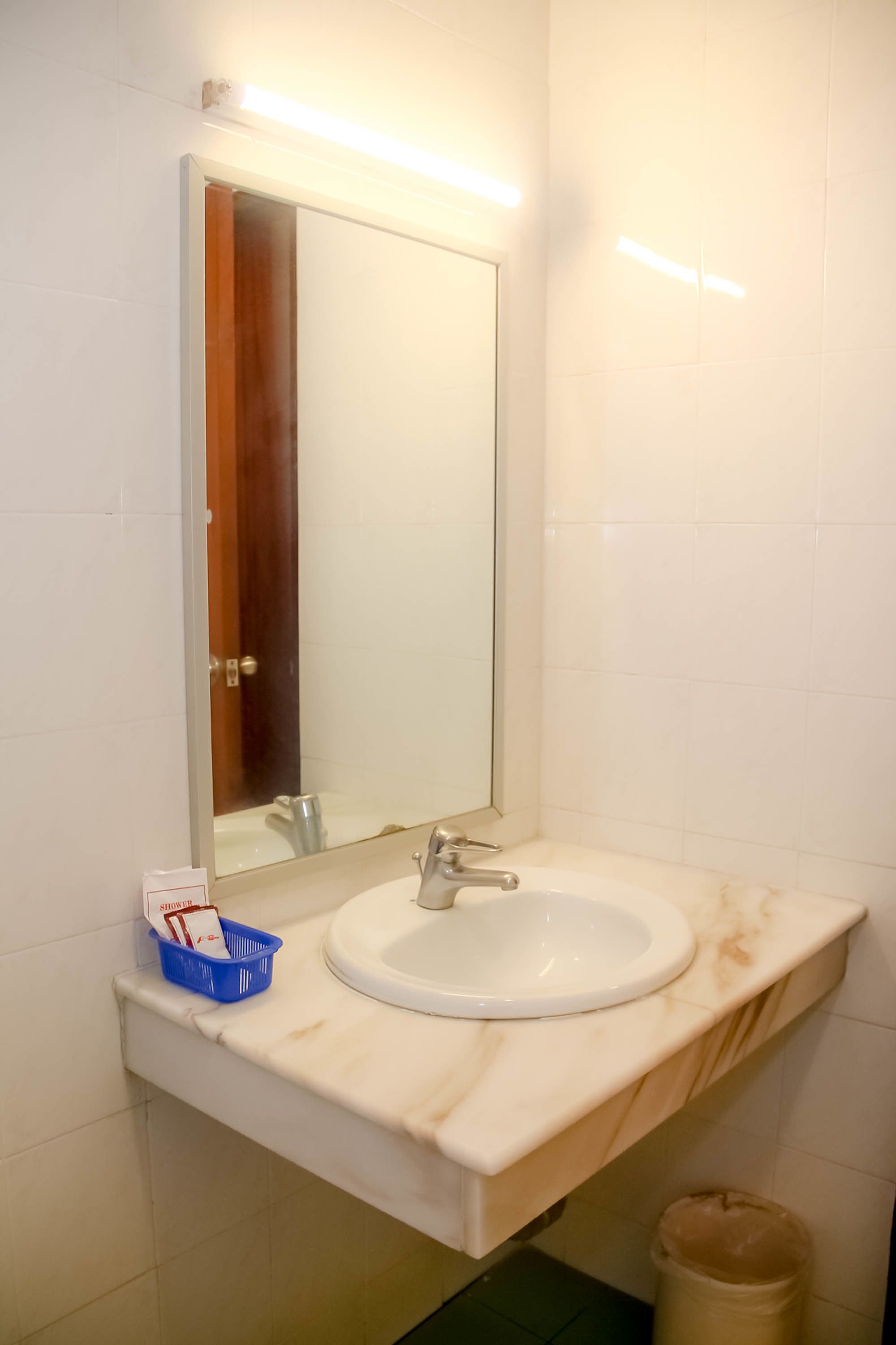 Une salle de bain avec un lavabo blanc, un miroir et un panier bleu posé sur le comptoir.