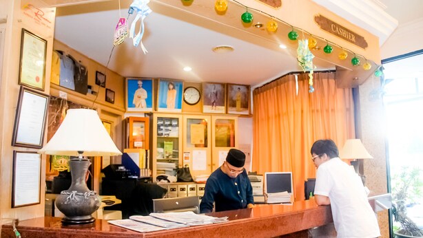 Een hotel receptiebalie met een man die erachter werkt, een klok en ingelijste foto's aan de muur.