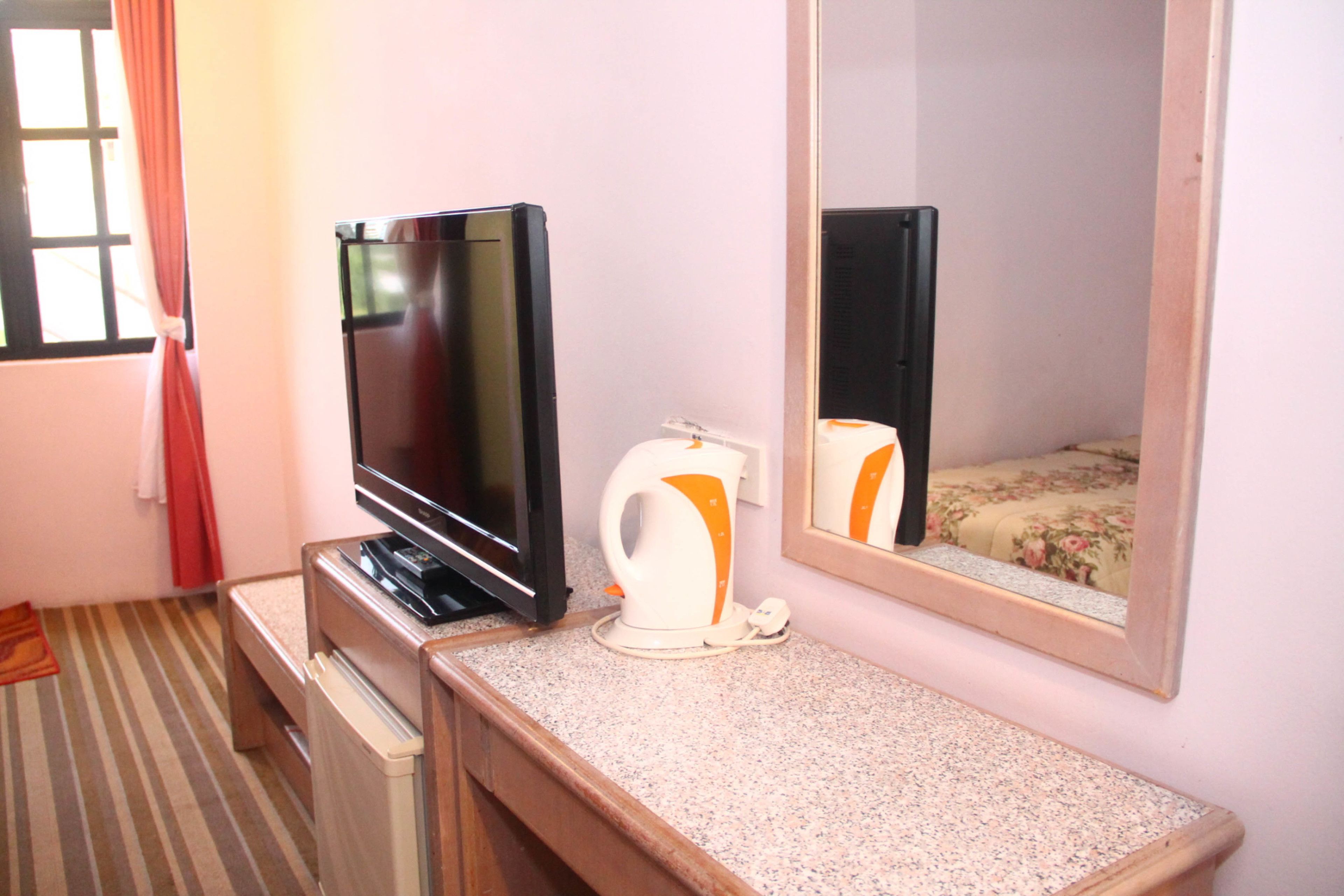 A hotel room with a television, a kettle, a mirror, and a bed with a floral bedspread.