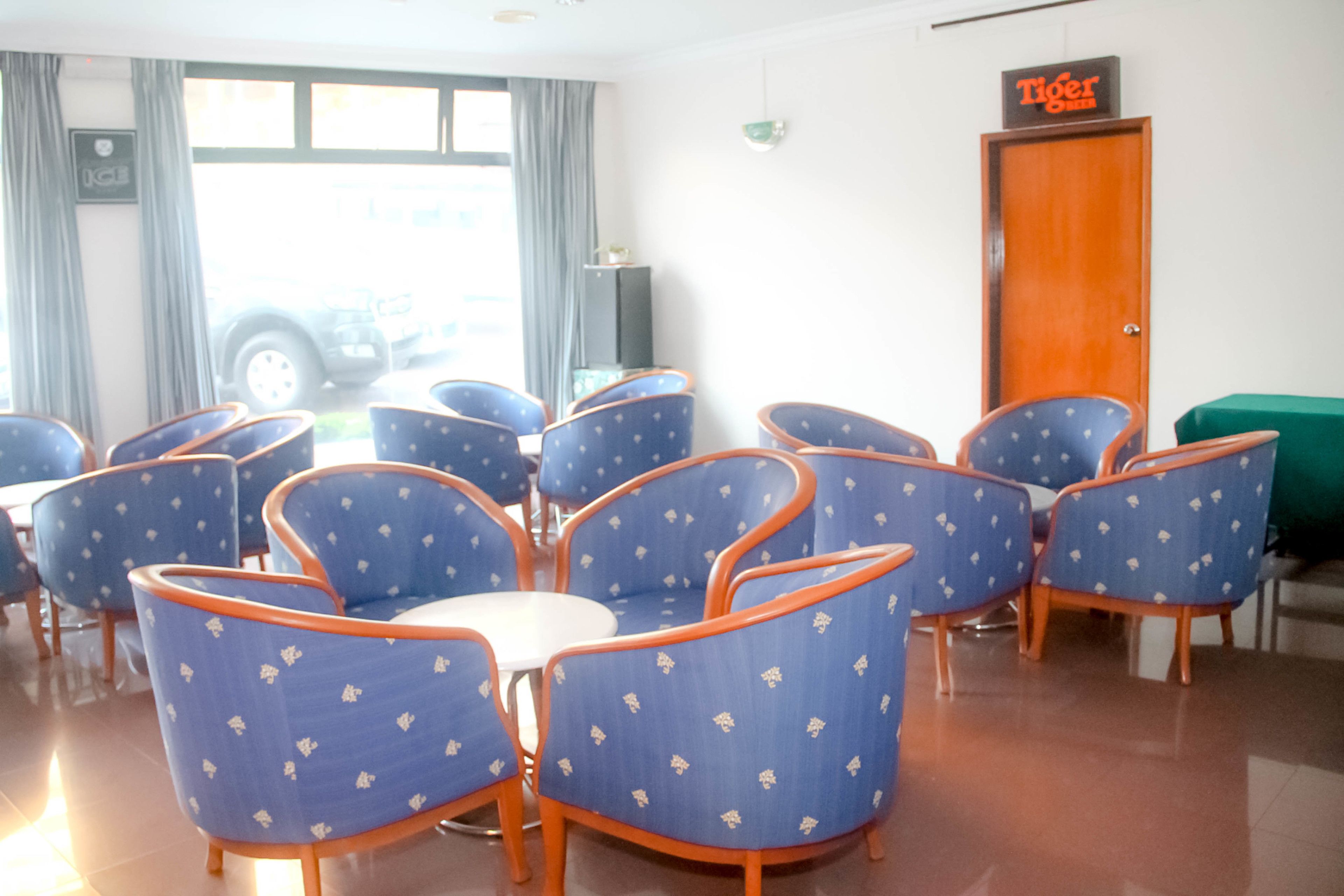 A room with several blue chairs with orange trim, a white table, and a green couch. There is a door labeled "Tiger" and a window with curtains.