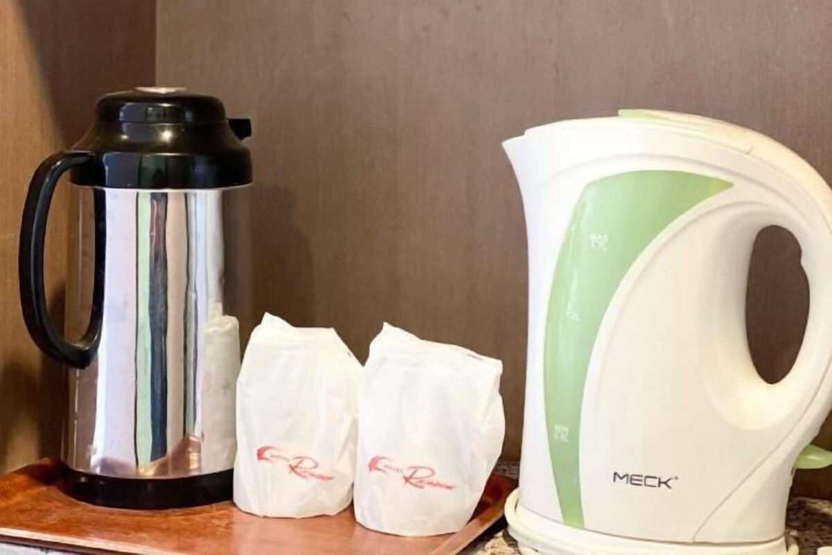 A kitchen area with a stainless steel coffee maker and a white electric kettle with a green stripe. There are three white paper bags with red text on the counter.