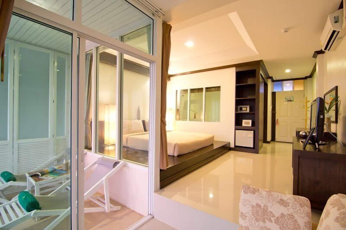 A modern hotel room with a sliding glass door leading to a balcony, a bed, a desk, and a small seating area.