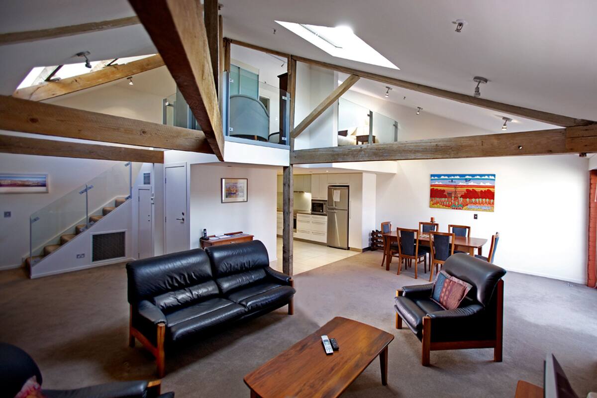 A spacious living area with a high ceiling, a sofa, a coffee table, and a dining area with chairs and a table.
