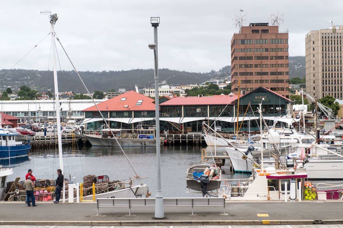 A marina with boats docked, a building with a red roof, and a tall building in the background.