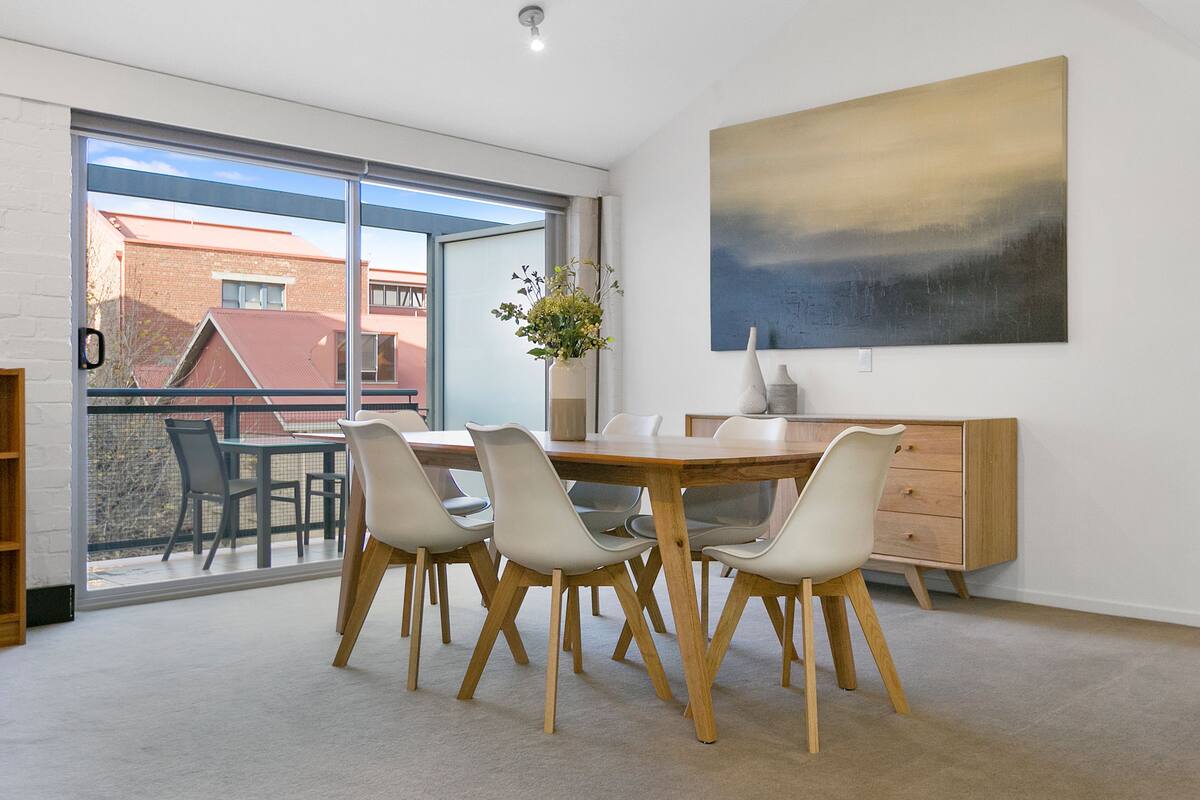 A dining area with a wooden table and chairs, a vase with flowers, and a painting on the wall.
