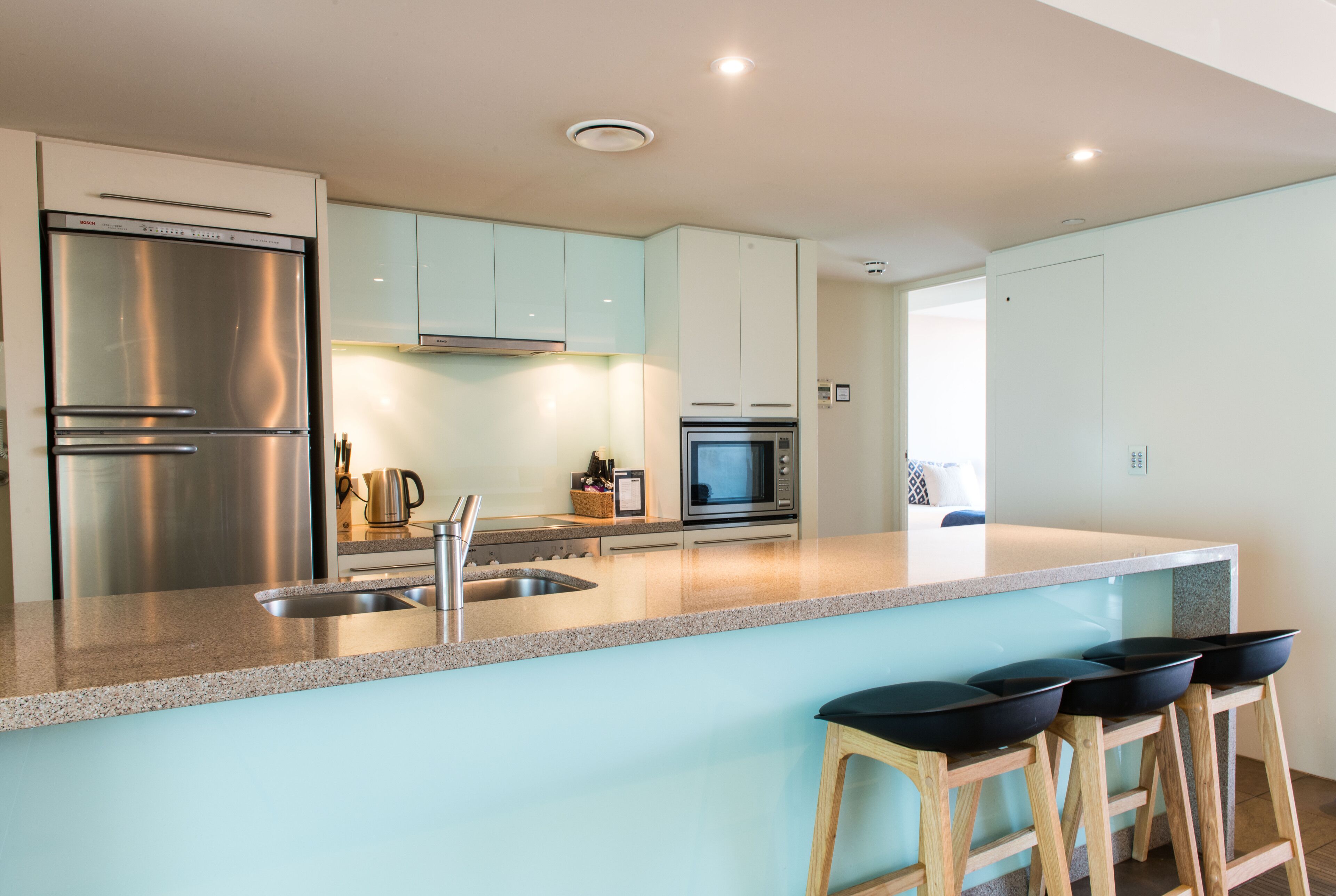 A modern kitchen with stainless steel appliances, a granite countertop, and bar stools.