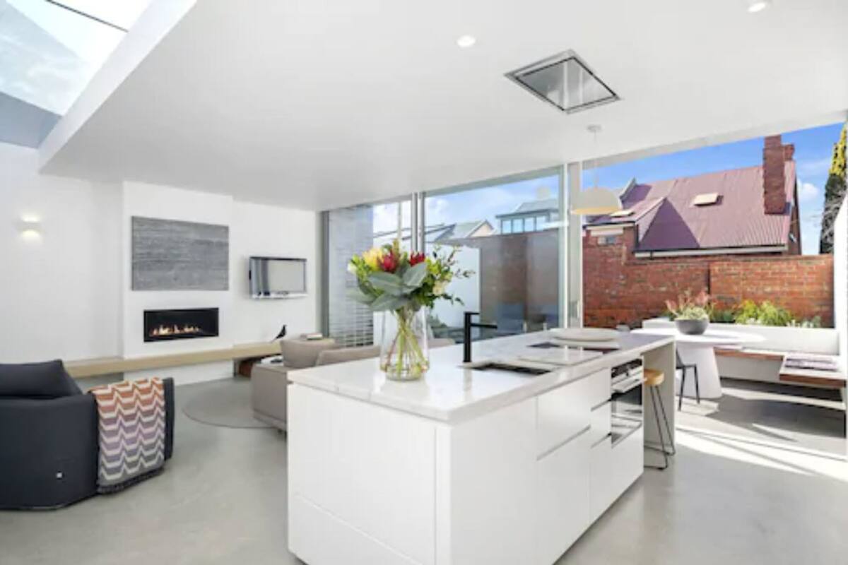 A modern kitchen with a central island, a fireplace, and large windows.