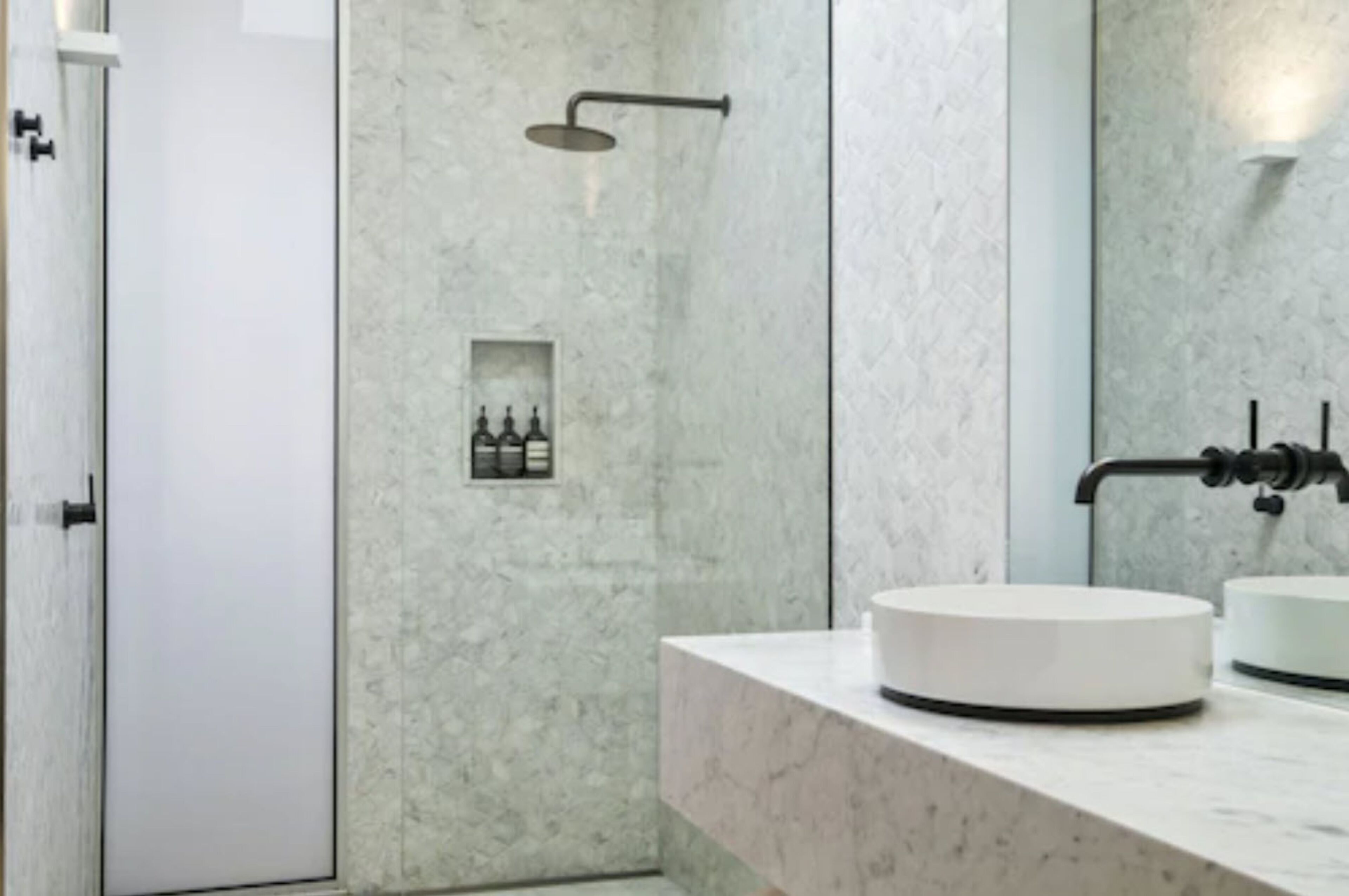 A modern bathroom with a round sink, a handheld showerhead, and a built-in shelf with toiletries.