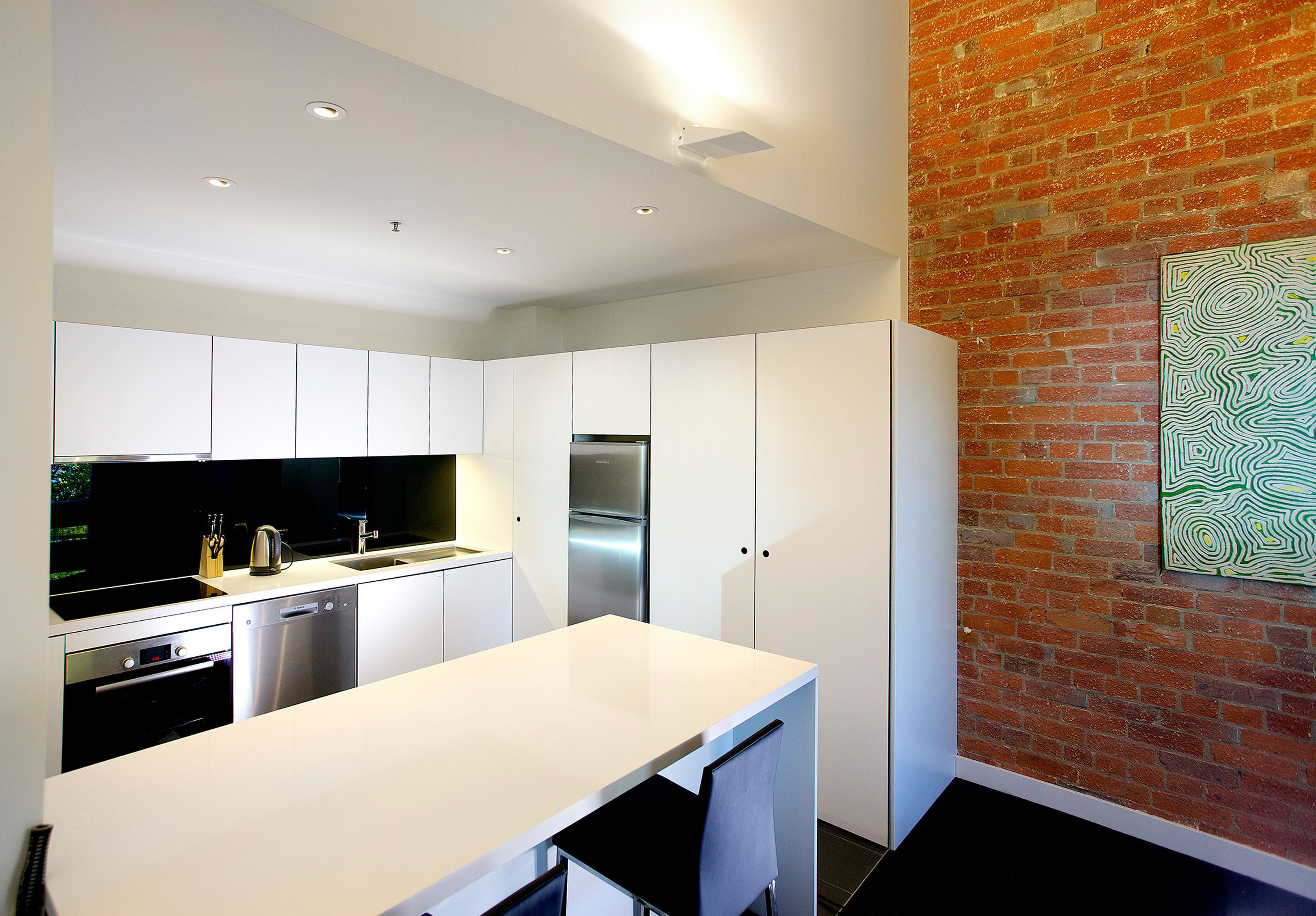 A modern kitchen with white cabinetry, stainless steel appliances, and a brick accent wall.
