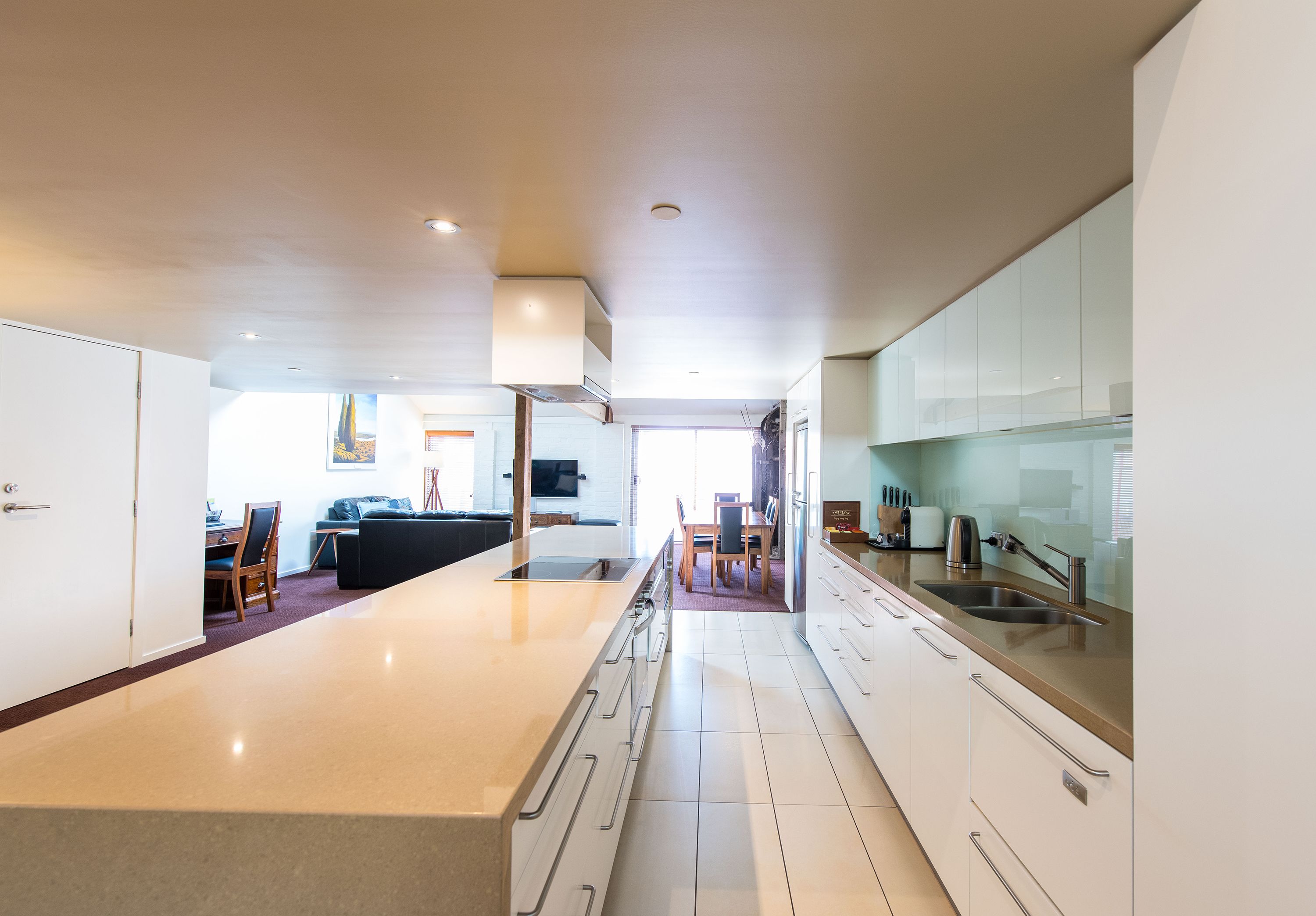A modern kitchen with a central island, white cabinetry, and a dining area in the background.