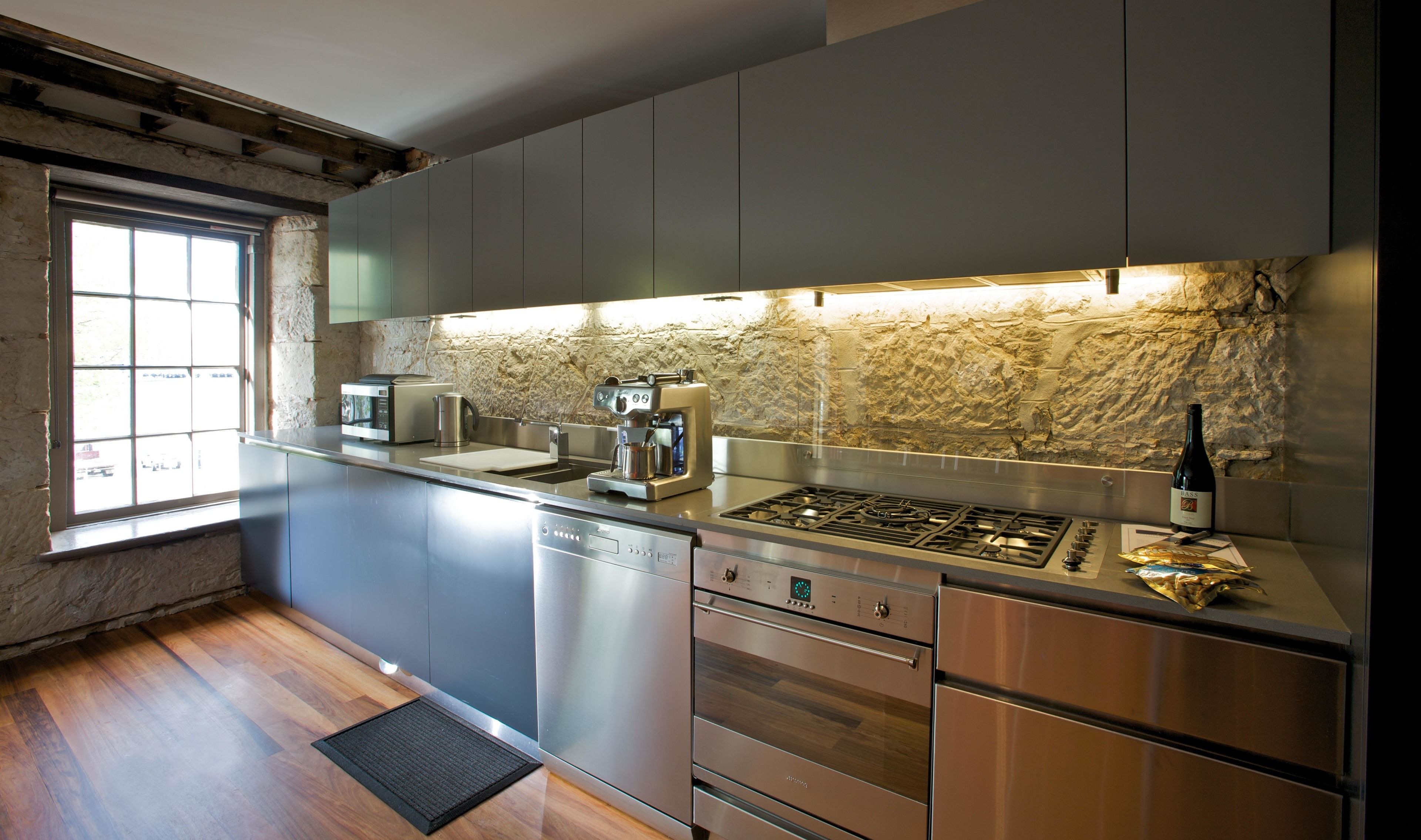 Una cocina moderna con electrodomésticos de acero inoxidable, protector contra salpicaduras de piedra y un ventanal que deja entrar luz natural.
