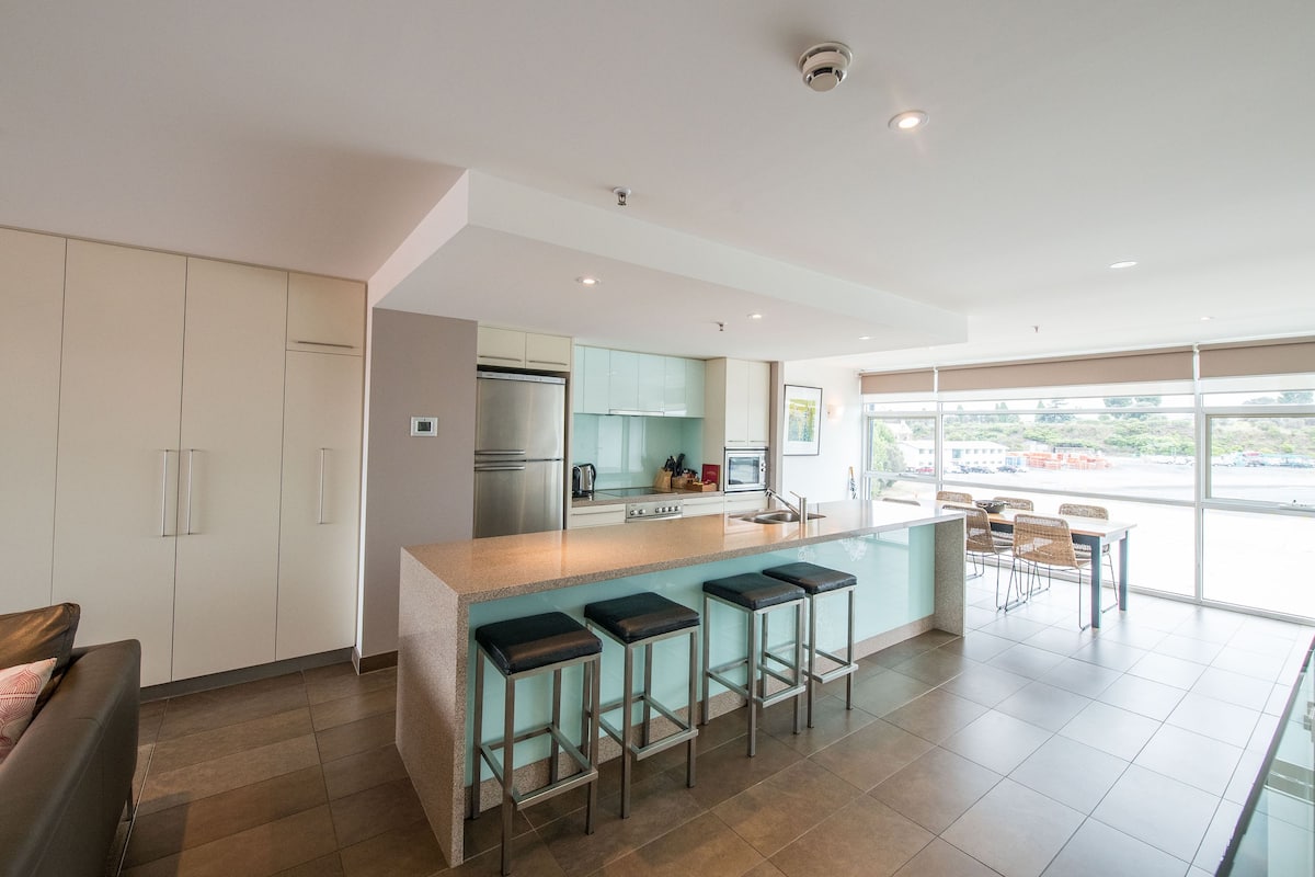 A modern kitchen with a central island, bar stools, and a dining area with chairs.