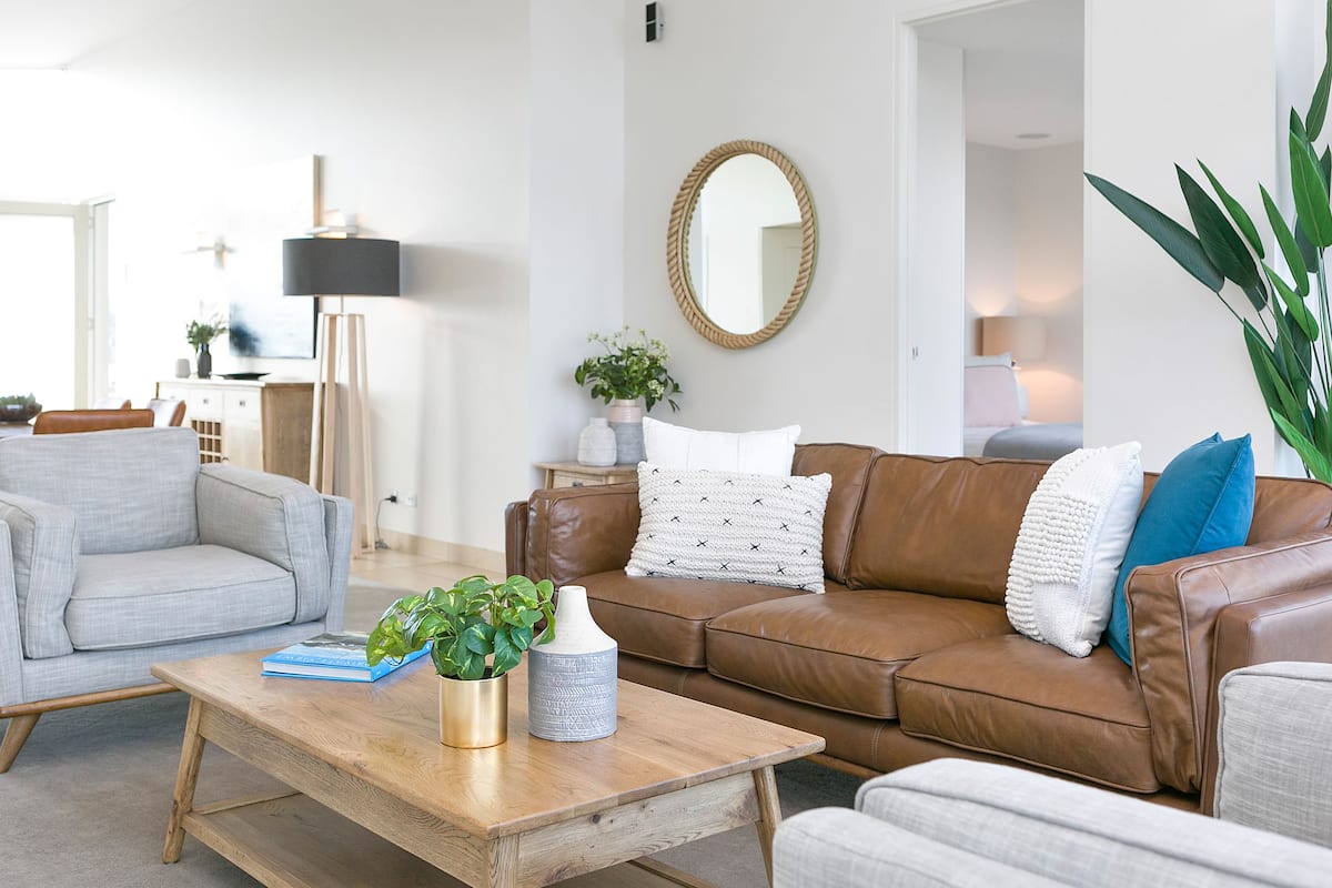 A modern living room with a brown leather sofa, a grey armchair, and a wooden coffee table.