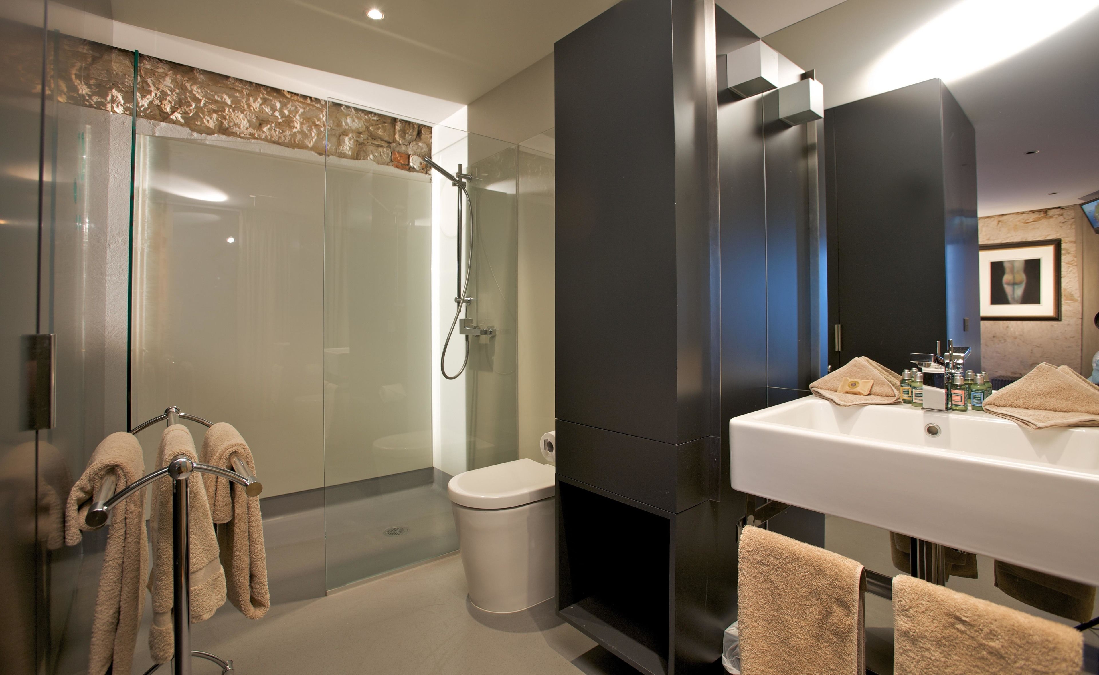 A modern bathroom with a glass-enclosed shower, a white sink with toiletries, and towels on a rack.