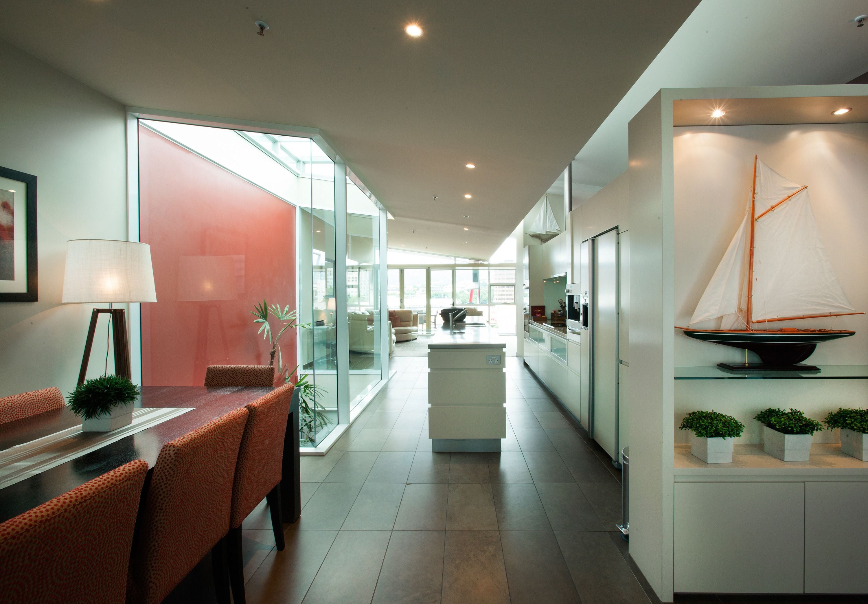 A modern kitchen with a dining area, a sailboat model, and a glass partition.