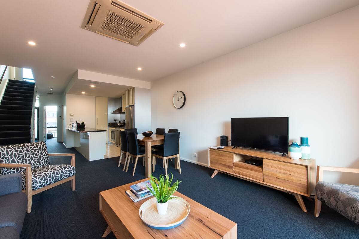 A modern living room with a sofa, coffee table, TV, and dining area.