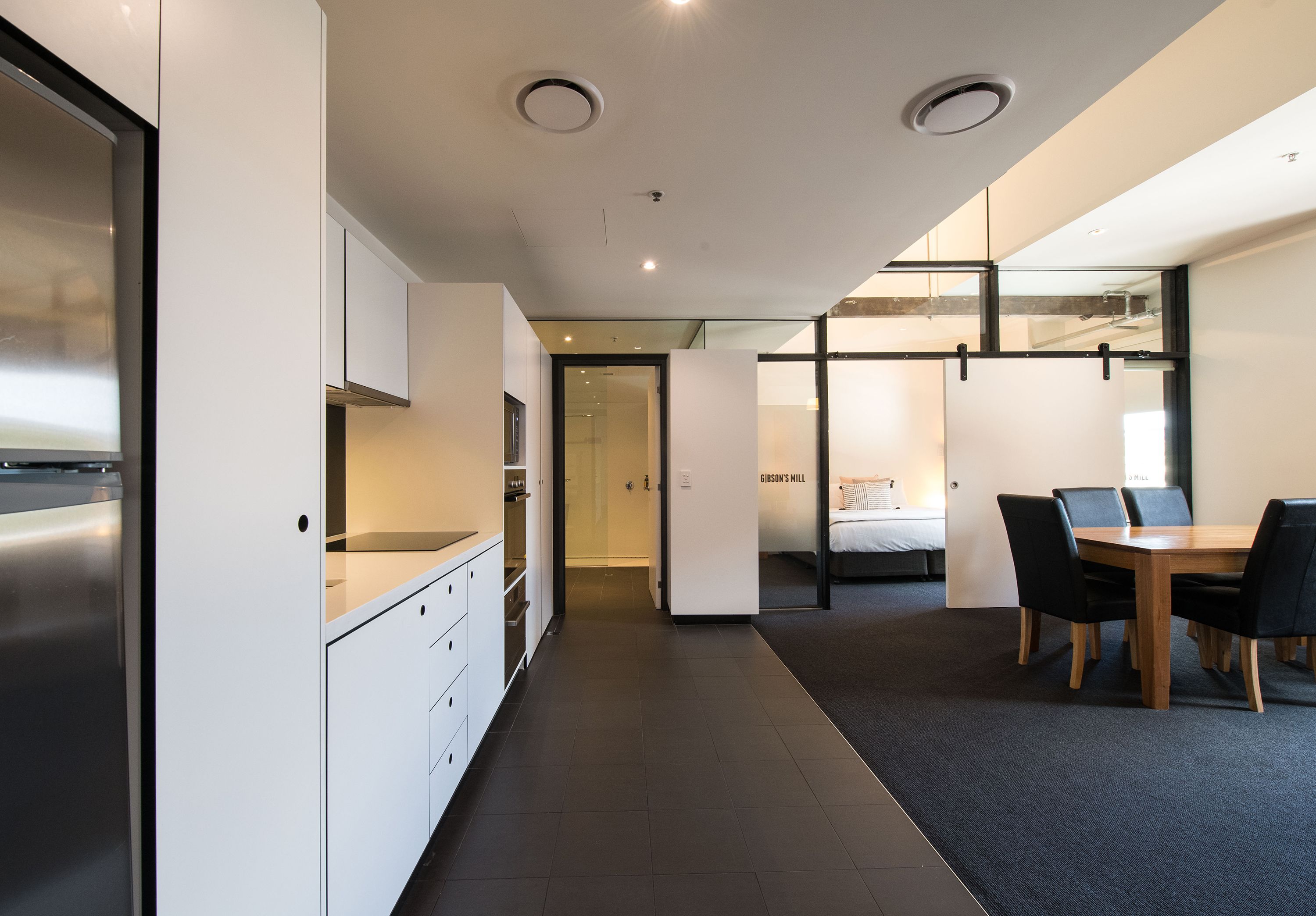 Una cocina moderna con armarios blancos, un refrigerador de acero inoxidable y un comedor con una mesa de madera y sillas negras.