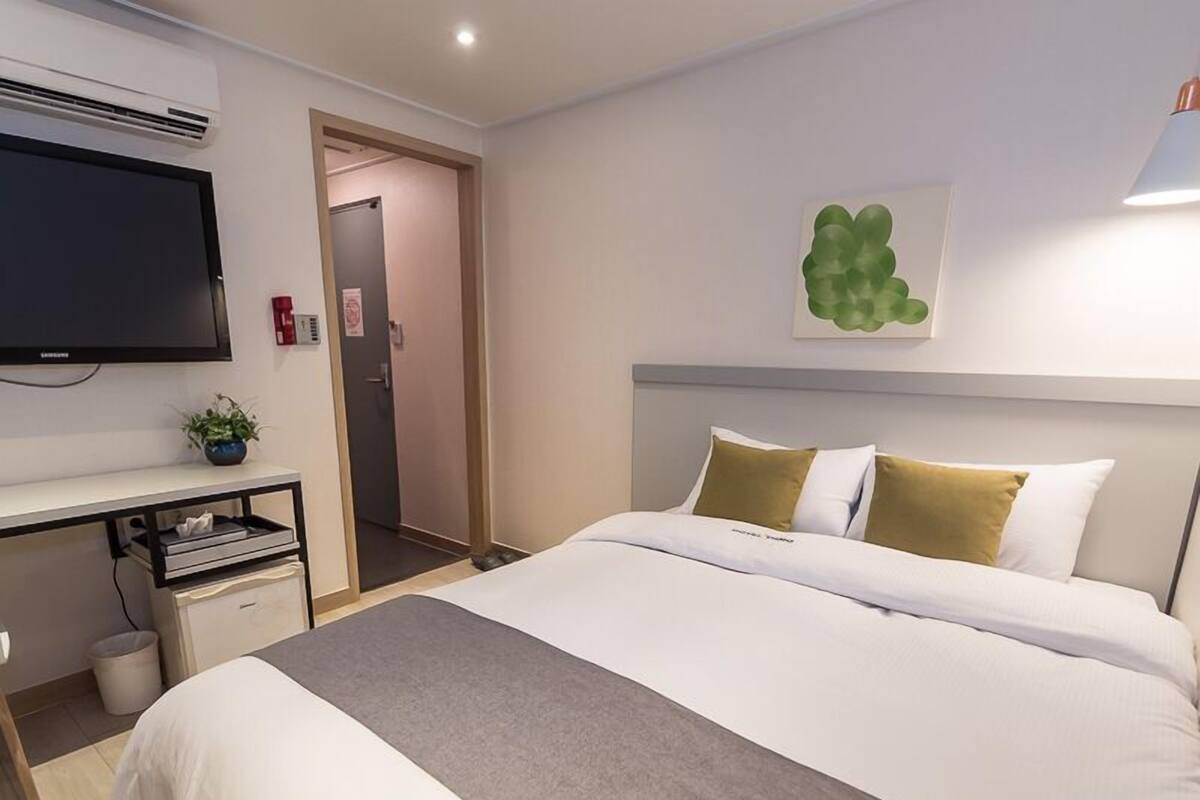 A hotel room with a bed, a desk, a television, and a green wall decoration.