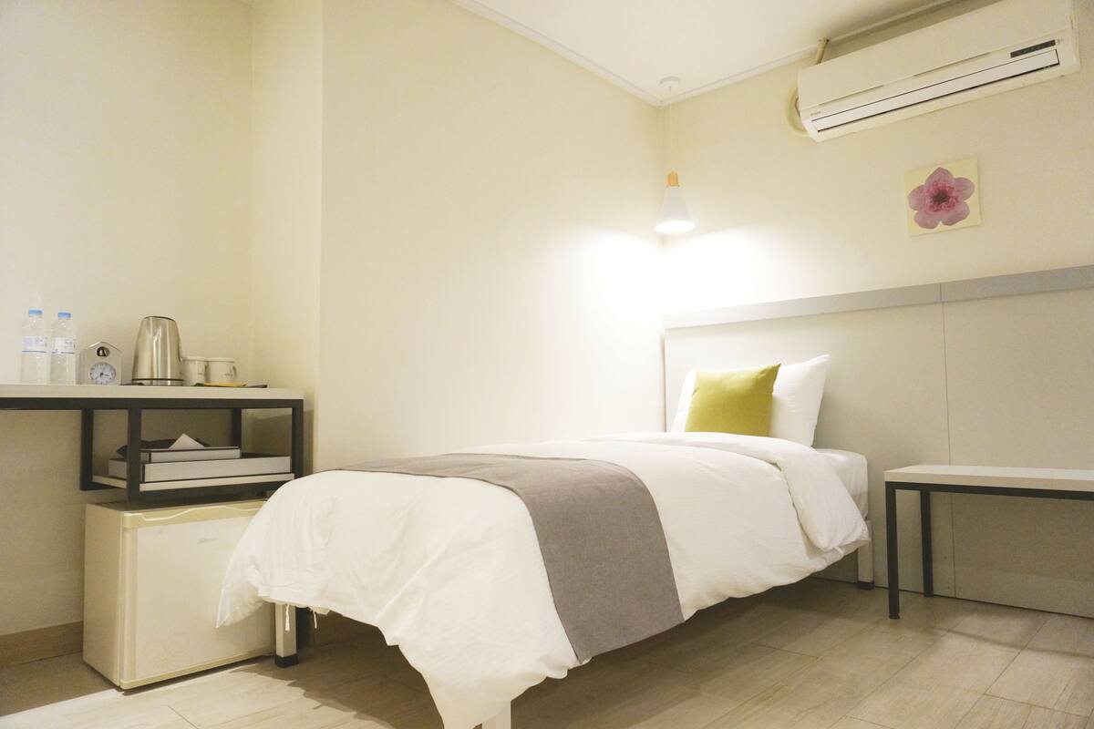 A neatly arranged hotel room with a bed, bedside table, and a small desk with a lamp.