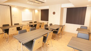 Ein Konferenzraum mit mehreren Tischen, Stühlen, einer Whiteboard und einer Projektionsleinwand.