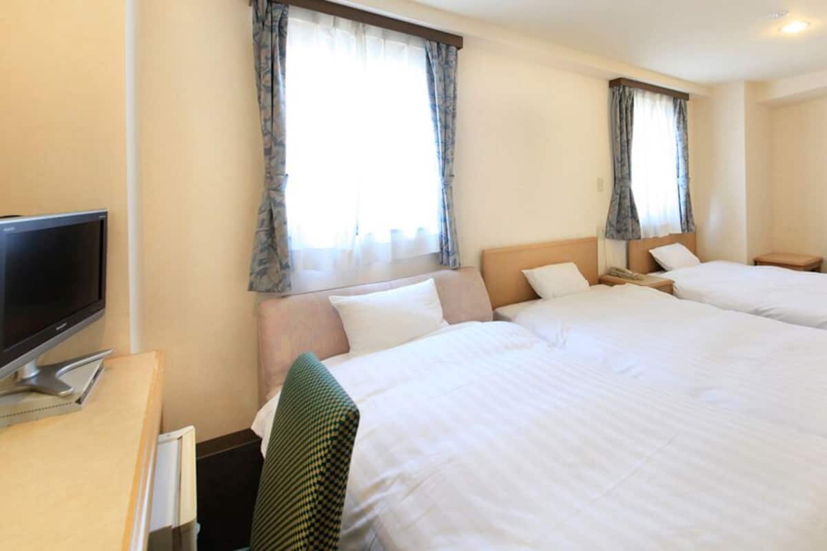 Quarto de hotel com duas camas, uma mesa de escritório com um computador e uma televisão.