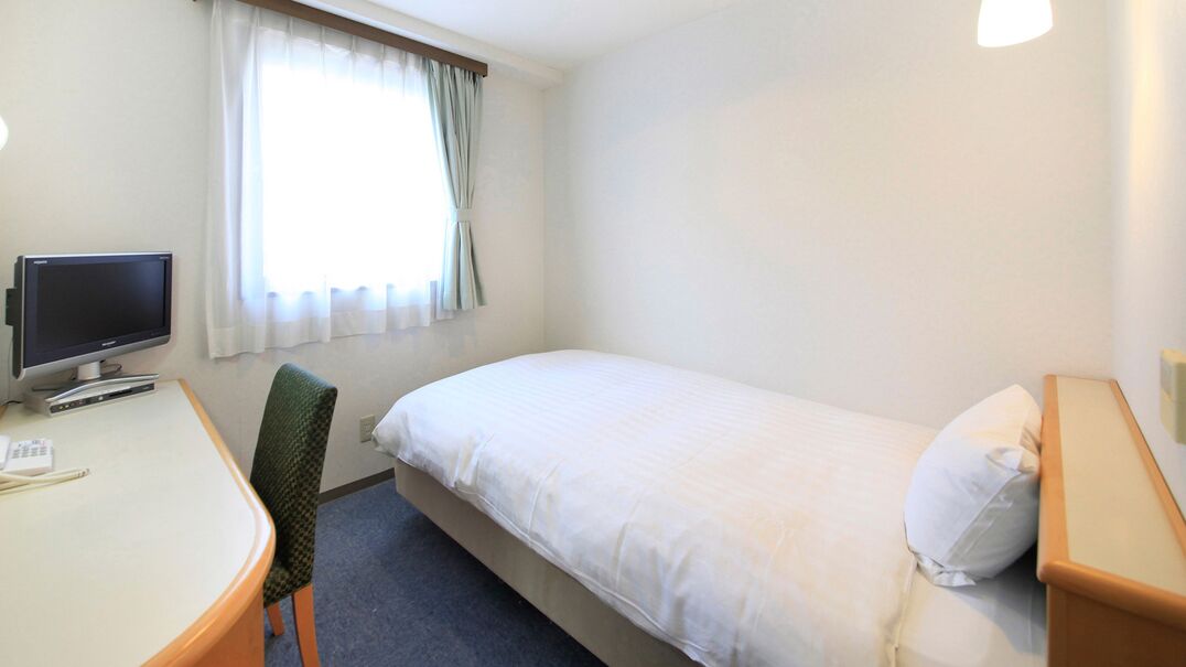 Una habitación de hotel con cama, escritorio con computadora, una silla y ventana con cortinas.