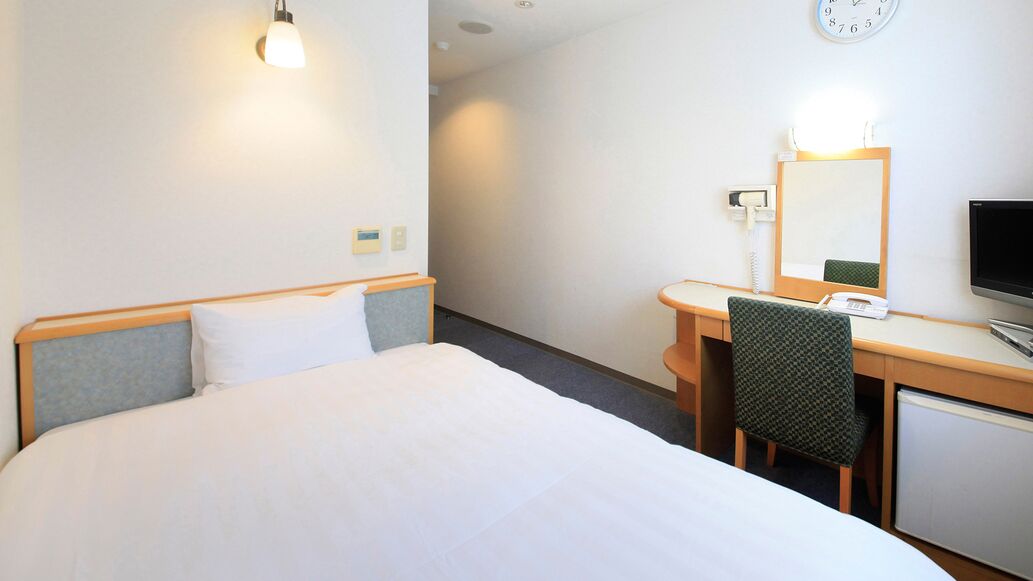 Una habitación de hotel con cama, escritorio, silla, televisión, espejo y un reloj en la pared.
