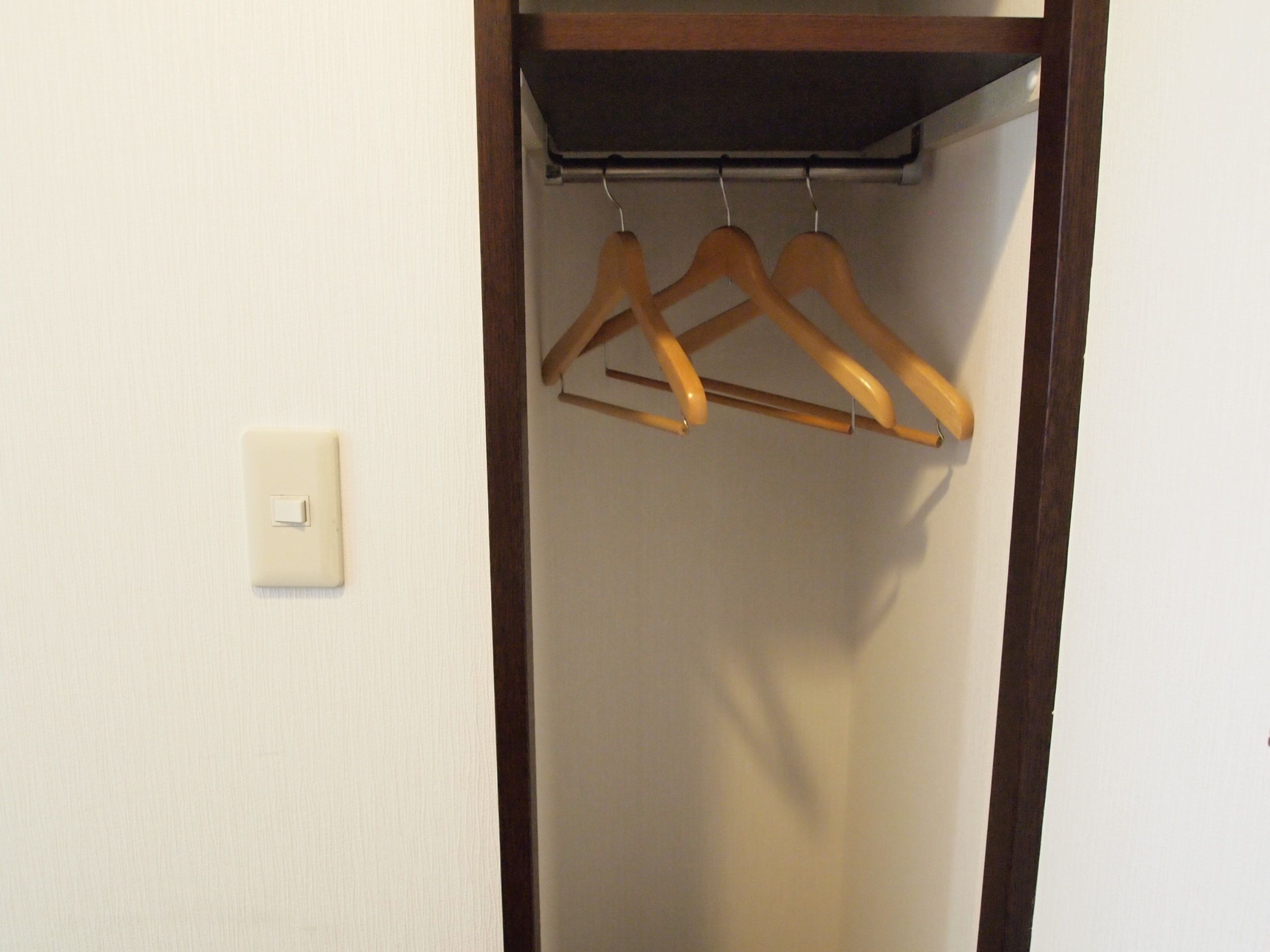 A closet with wooden hangers and a light switch on the wall.