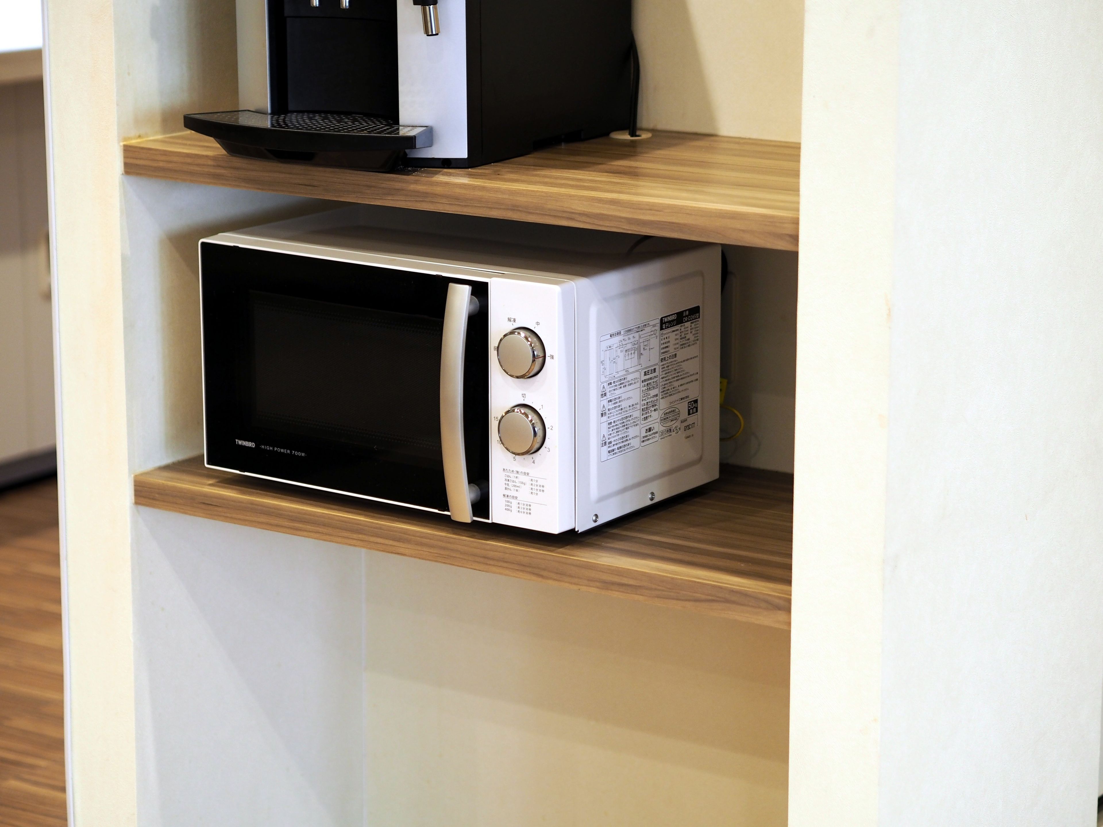 A microwave oven on a wooden shelf in a kitchen.