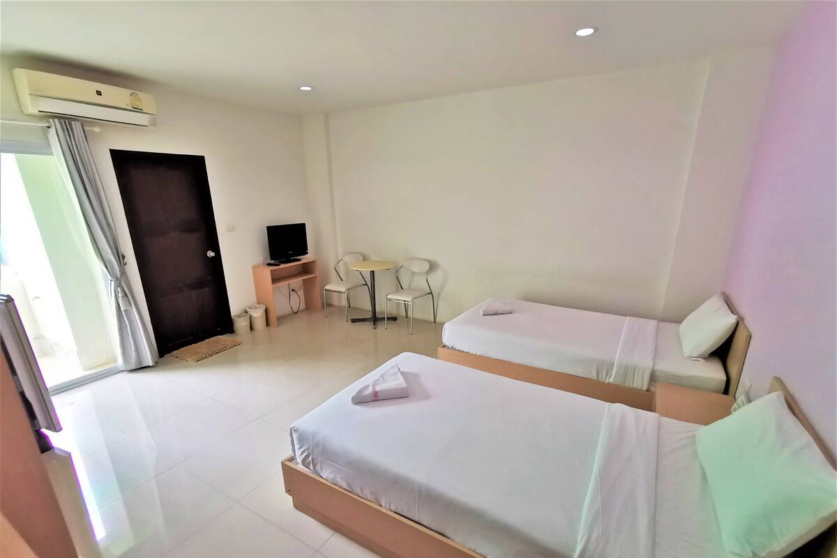 A hotel room with two beds, a desk with a chair, a television, and a window with curtains.