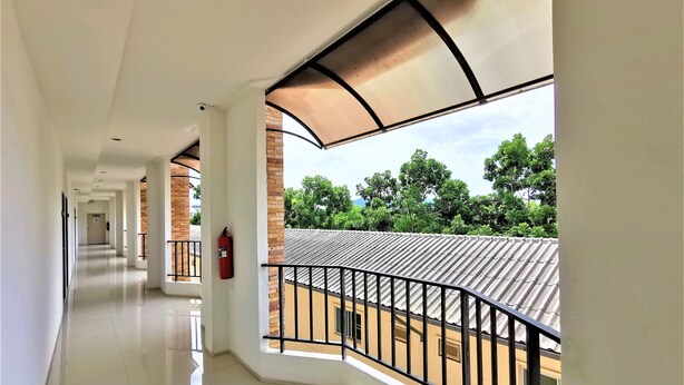 A corridor with a fire extinguisher, a balcony with a metal railing, and a view of trees and buildings. - Hua Hin Irooms Hotel (Hua Hin)