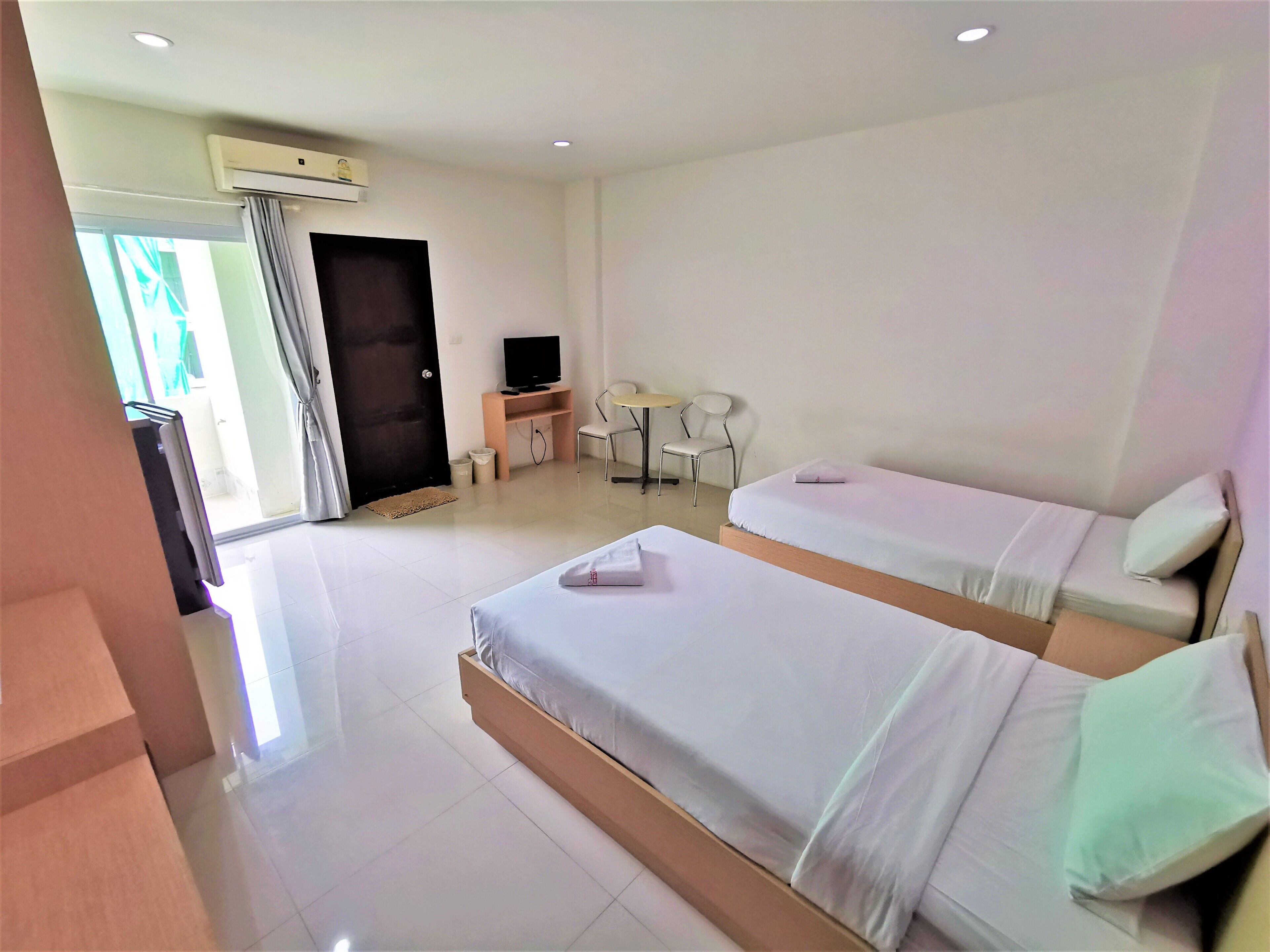 A hotel room with two beds, a desk with a chair, a TV, and an air conditioning unit.
