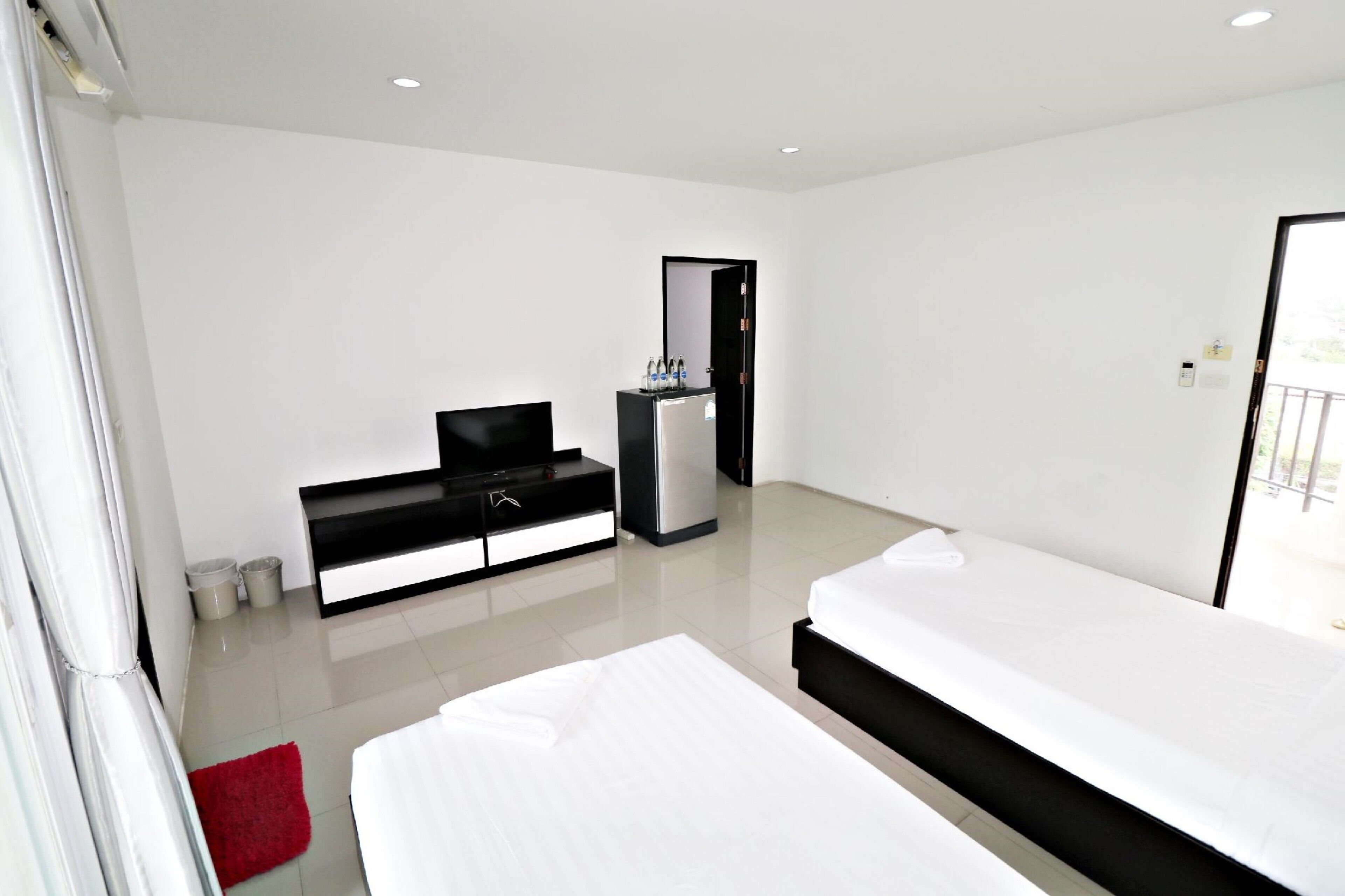 A modern hotel room with a large bed, a TV, a minibar, and a bathroom visible through an open door.