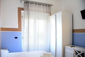 Ein Hotelzimmer mit Bett, Schreibtisch, Stuhl, Kleiderschrank und an der Wand befestigtem Fernseher.