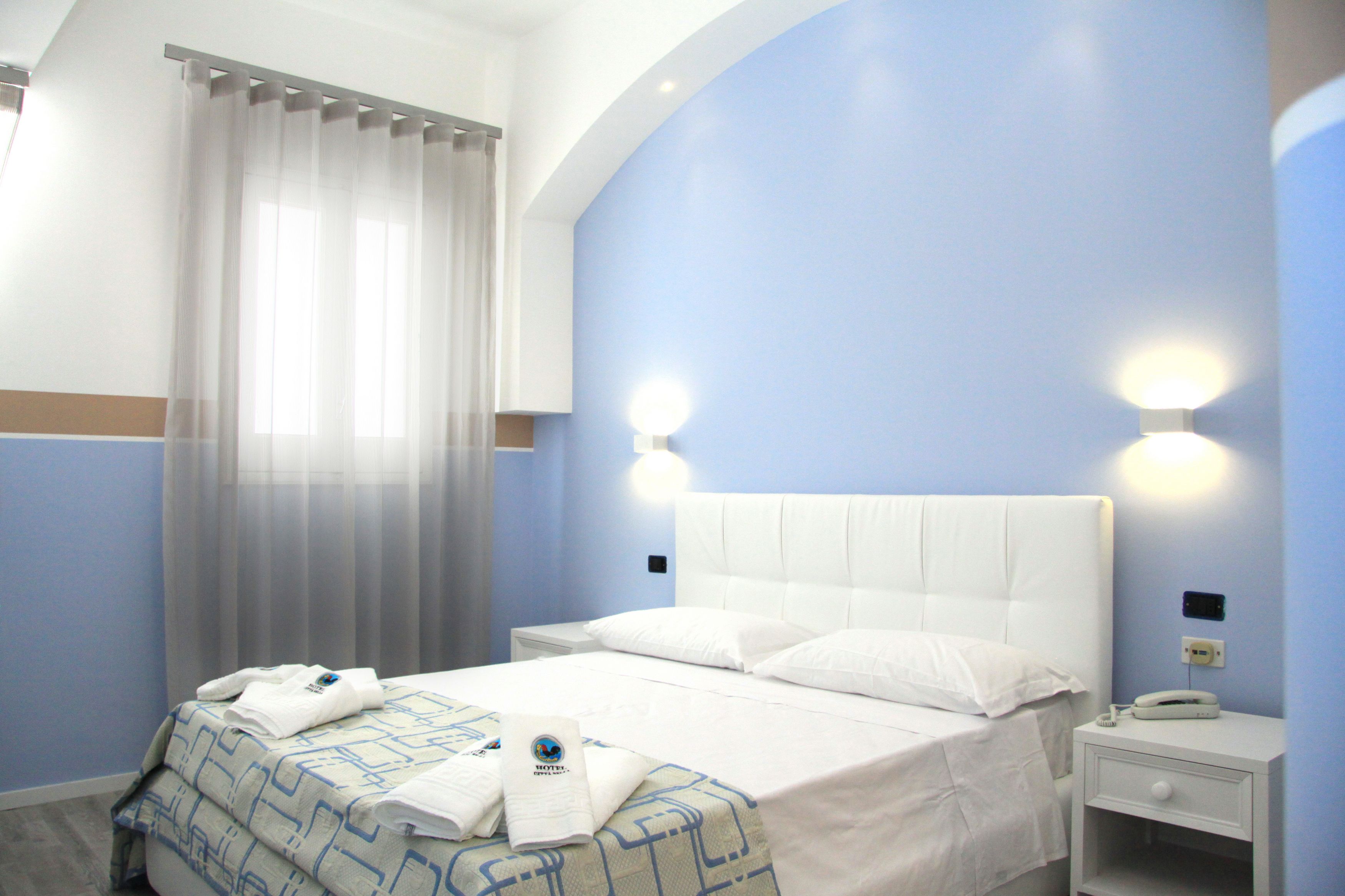 Una habitación de hotel con una cama, una mesita de noche, un teléfono y una ventana con cortinas.