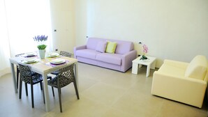 A living room with a dining table set for four, a light purple sofa, and a white sofa. - Hotel Città Bella (Gallipoli)