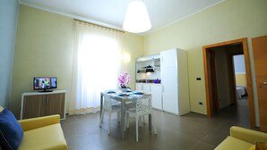 A compact living space with a dining area, kitchenette, and a television. - Hotel Città Bella (Gallipoli)