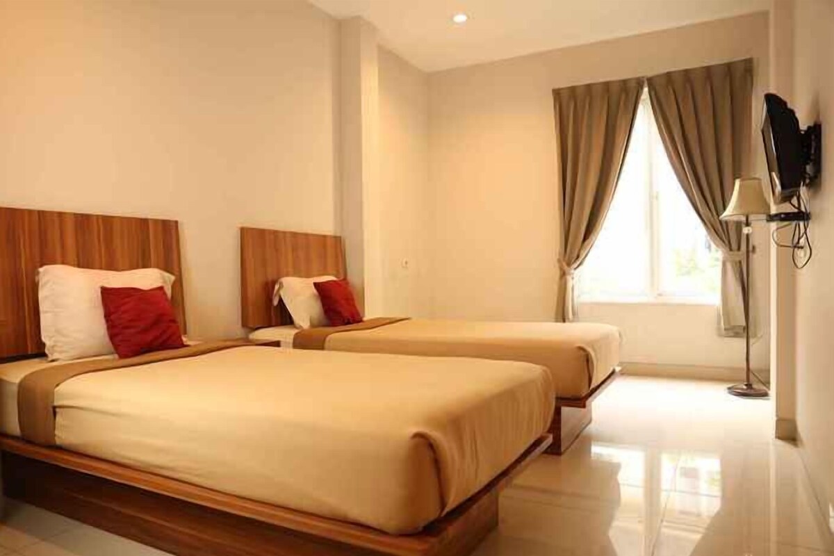 A hotel room with two beds, a TV, and a window with curtains.