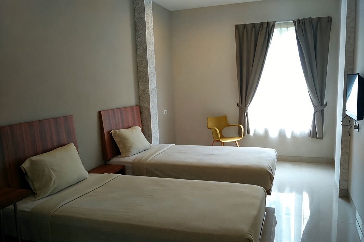 A hotel room with two beds, a chair, and a television.