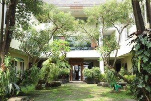 A courtyard with a central pathway, surrounded by lush greenery and a building with a balcony.