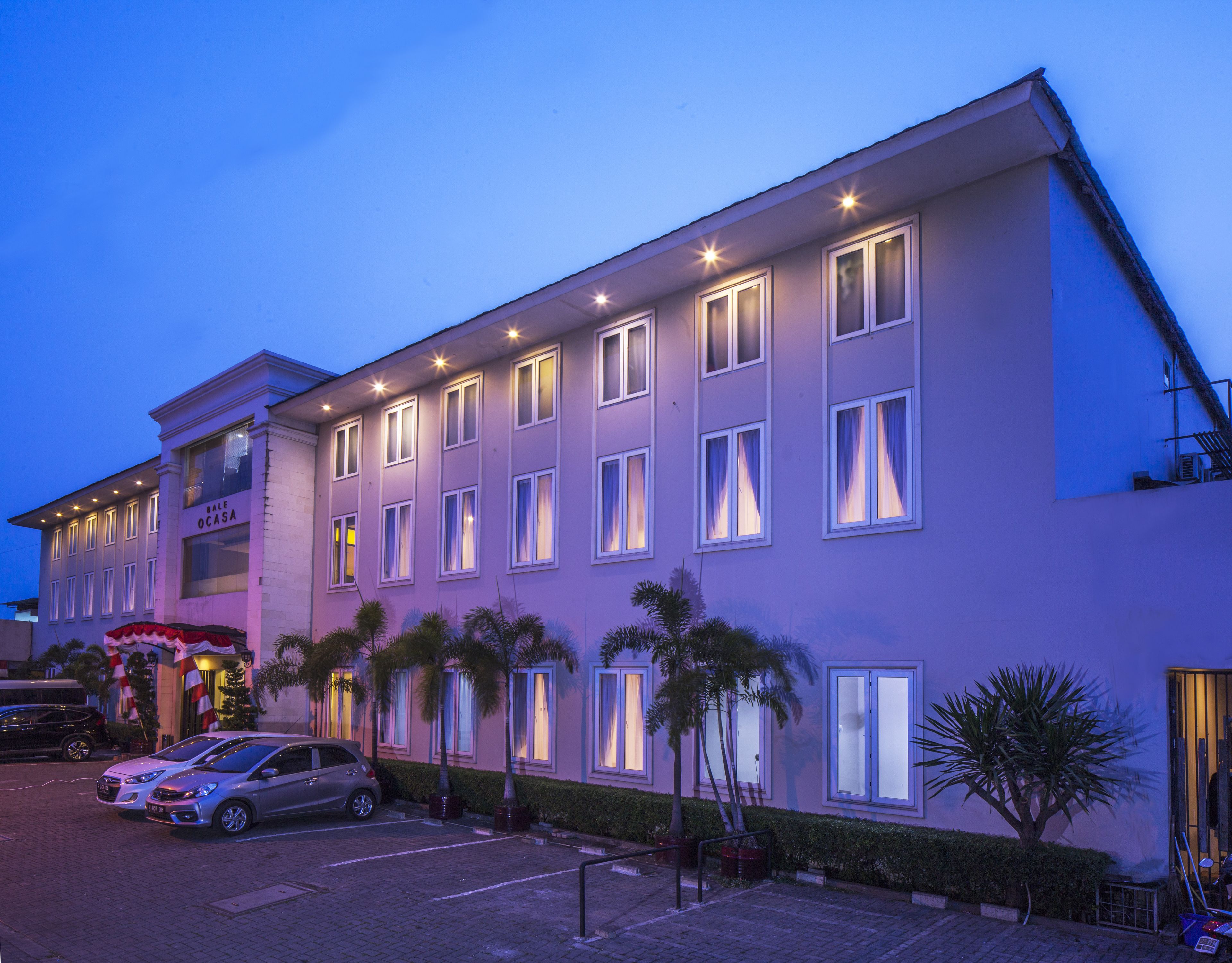 A multi-story hotel with a flat facade, multiple windows, and a parking area with cars.